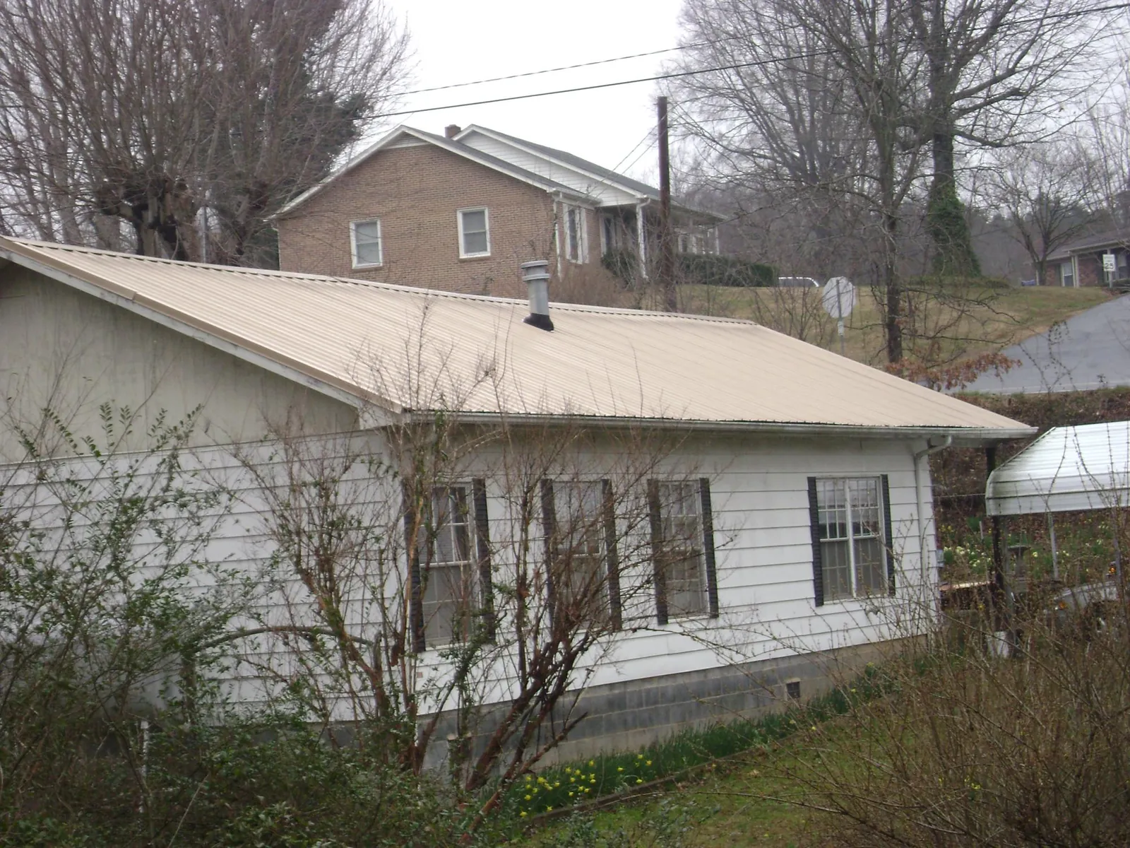 Tan metal roof on a white sided house set into a hillside — Commercial Roofing by Roofing Brothers in Tahoma